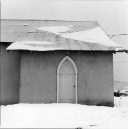 A snow-covered building with a pointed arch door and patches of snow on the slanted roof.