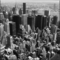 Aerial view of Manhattan skyscrapers in black and white, with the East River visible in the background.