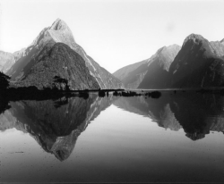 Black and white photo of mountains reflected in a calm lake, with clear sky and still water.