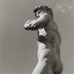 Black and white photo of Michelangelo's David statue viewed from below, showing the back and left side.