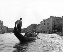 A gondolier steers a gondola with passengers along a canal lined with historic buildings in Venice, Italy.