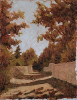 A dirt pathway bordered by stone walls and trees with autumn foliage under a clear sky.