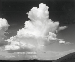 Large cumulus clouds float above a distant horizon and low hills under a mostly clear sky.