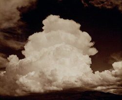 Large cumulus clouds fill the sky, with dark land visible at the bottom of the image.