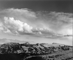 Snow-capped mountain range under a dramatic sky with large, textured clouds.