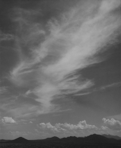 Black-and-white photo of wispy clouds stretching across the sky above a distant mountain range.
