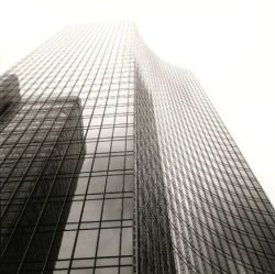 Tall glass skyscraper with a grid pattern of windows, photographed from a low angle against a pale sky.