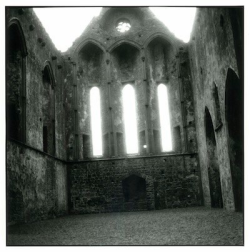 Interior of an old, roofless stone church with tall, narrow windows and a gravel floor.