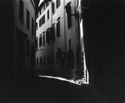 Narrow, shadowed alley with sunlight illuminating a lone bicycle against a building wall.