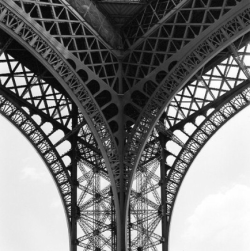 Close-up view of the iron lattice structure under the Eiffel Tower, showing intersecting beams and supports.