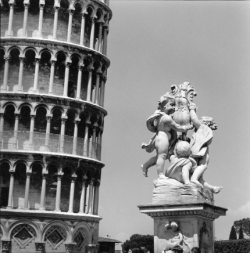 Leaning Tower of Pisa on the left, marble statue of cherubs with a shield on the right, under a clear sky.