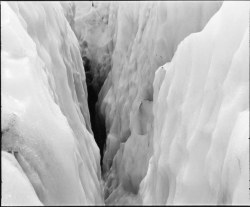 A narrow crevasse cuts through thick, jagged ice, forming a deep gap between icy walls.