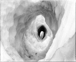 A tunnel-like hole in a mass of ice, showing layered, spiraling walls and an opening at the far end.